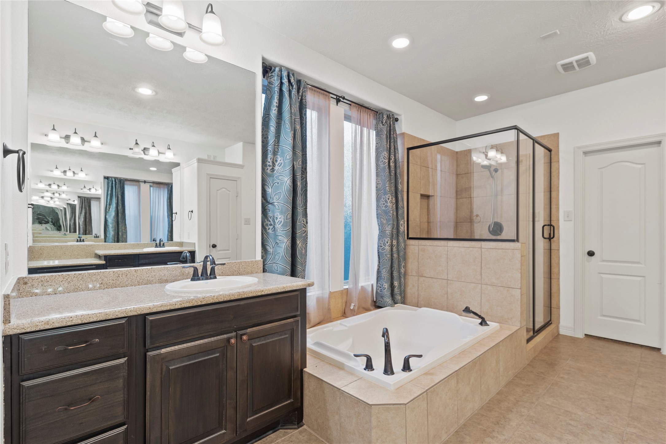 5827 Amherst Farms Lane Fulshear, TX 77441 - Photo 19 of 48 The en-suite bathroom delivers a spa-inspired experience with a large soaking tub and separate spacious glass-enclosed shower with neutral tile. The vanity features granite countertops, dark wood cabinetry, and oil-rubbed bronze fixtures, offering both beauty and functionality.