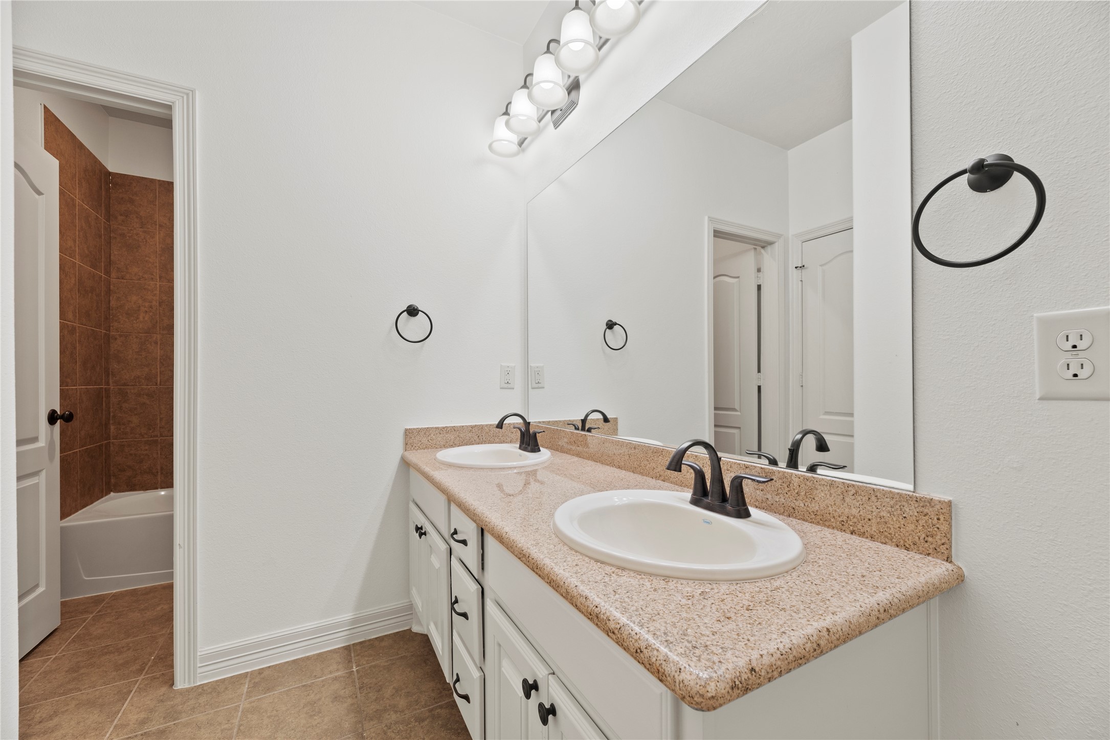5827 Amherst Farms Lane Fulshear, TX 77441 - Photo 26 of 48 This well-appointed secondary bathroom features a long granite countertop with dual undermount sinks and ample cabinetry for storage. A full-width mirror enhances brightness, while updated light fixtures provide balanced illumination. The neutral tile flooring complements the warm granite tones for a cohesive finish.