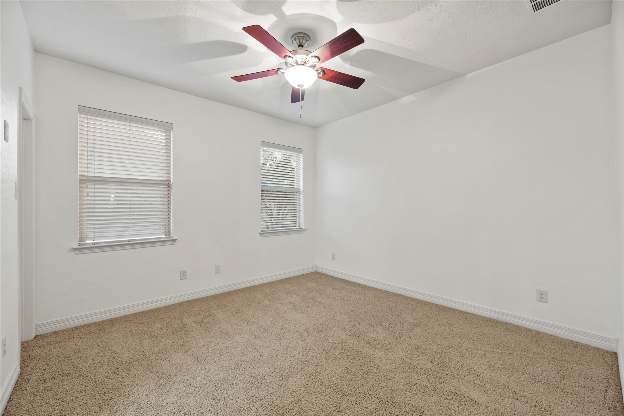 5827 Amherst Farms Lane Fulshear, TX 77441 - Photo 27 of 48 Another spacious bedroom offers two windows that fill the space with natural light. Decorative curtain rods add character, while the neutral color palette allows for versatile styling. Plush carpeting and a ceiling fan complete this inviting space.
