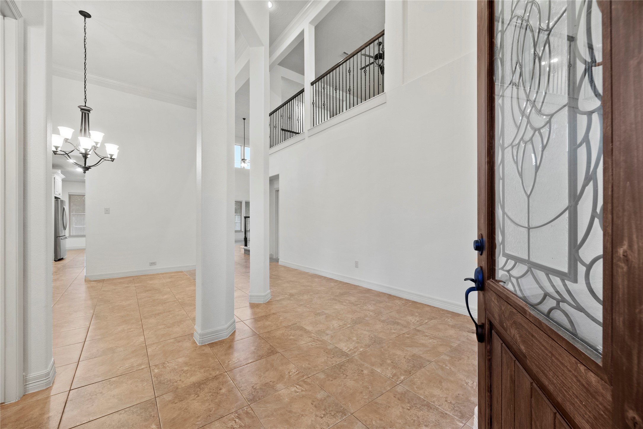 5827 Amherst Farms Lane Fulshear, TX 77441 - Photo 3 of 48 Step inside through the richly stained wood front door featuring decorative leaded glass and into a dramatic two-story foyer. Soaring ceilings, crisp white walls, and oversized tile flooring create an immediate sense of openness and light.