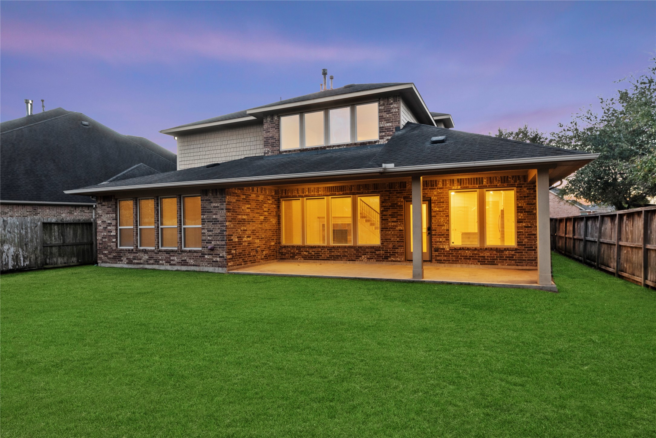 5827 Amherst Farms Lane Fulshear, TX 77441 - Photo 32 of 48 A stunning twilight view showcases the home’s full brick rear elevation, beautifully illuminated by warm interior lighting. This angle emphasizes the depth of the covered patio.