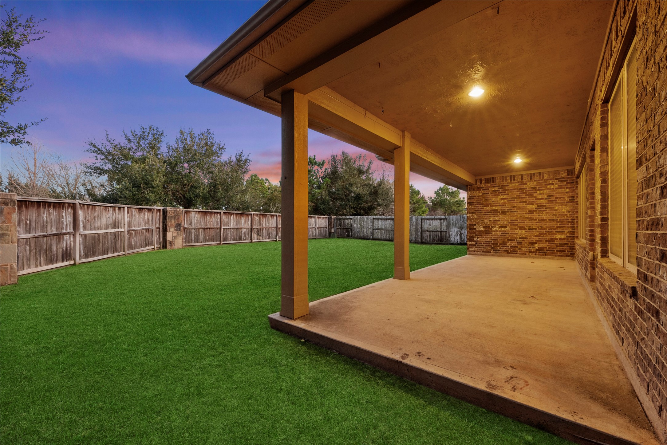 5827 Amherst Farms Lane Fulshear, TX 77441 - Photo 35 of 48 From beneath the covered patio, this view showcases the wide-open backyard framed by mature trees beyond the fence line. The extended concrete surface provides generous entertaining space, while the privacy fencing creates a secluded retreat perfect for outdoor living year-round.
