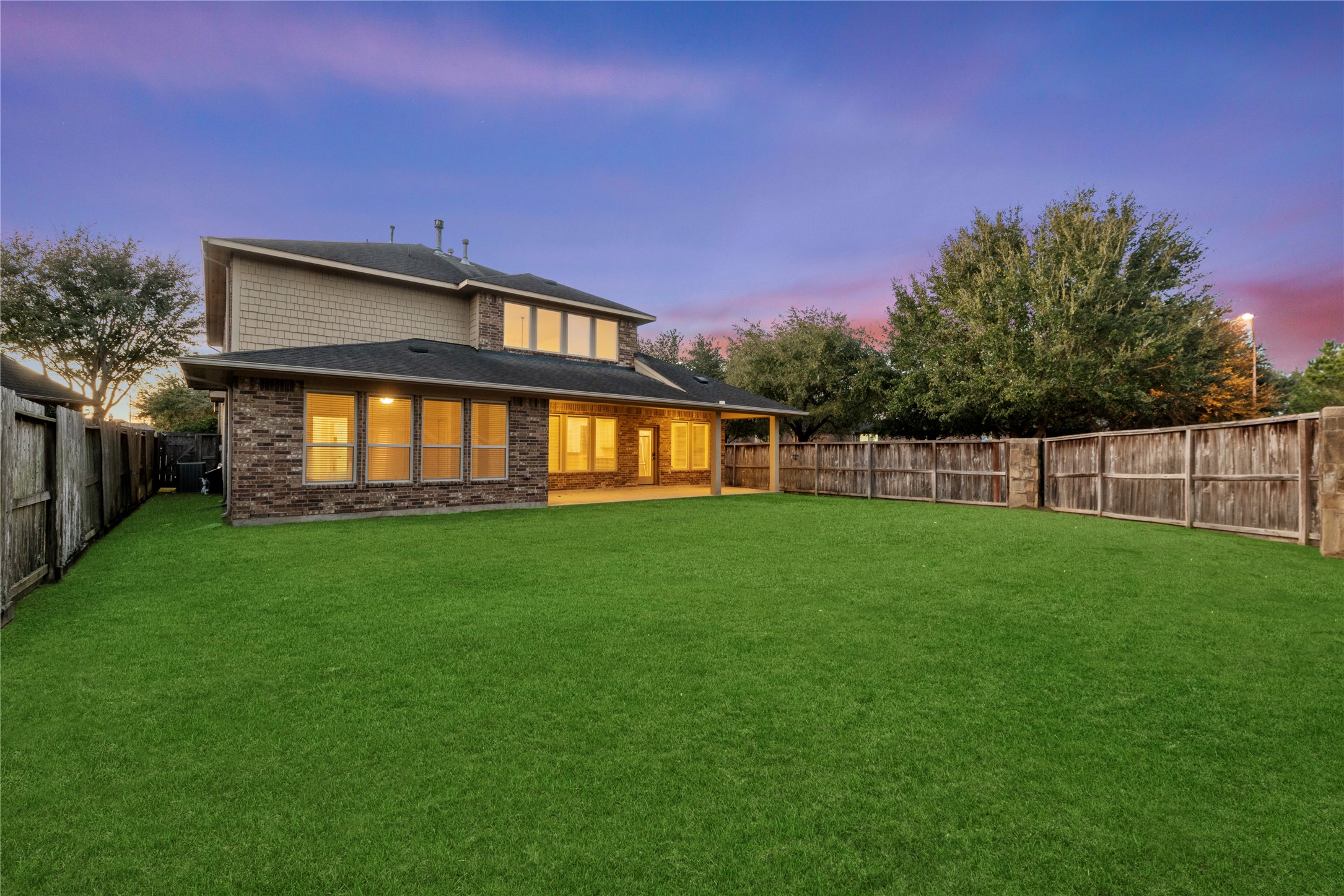 5827 Amherst Farms Lane Fulshear, TX 77441 - Photo 36 of 48 This wide-angle twilight shot captures the impressive size of the backyard and the welcoming glow from the home’s interior. The expansive green lawn offers endless possibilities for customization, from a future pool to a play area or garden oasis. The fully fenced yard ensures privacy while maintaining an open, airy feel.