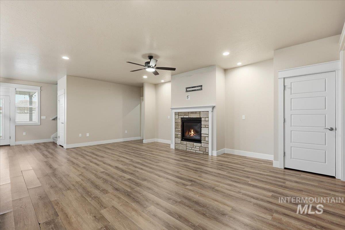 92 South Ravine Way Nampa, ID 83687 - Photo 12 of 29 Unfurnished living room with light wood-type flooring, a stone fireplace, recessed lighting, ceiling fan, and stairs