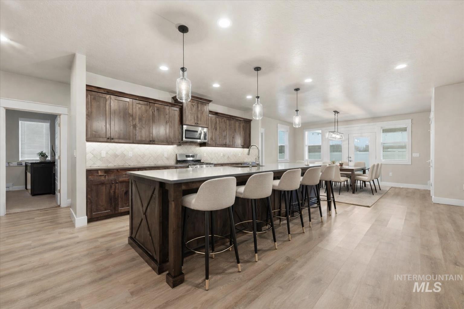 92 South Ravine Way Nampa, ID 83687 - Photo 6 of 29 Kitchen featuring a kitchen bar, hanging light fixtures, a kitchen island with sink, dark wood finish cabinetry, and light wood-type flooring
