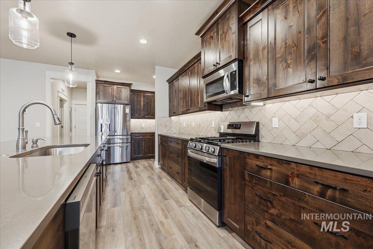 92 South Ravine Way Nampa, ID 83687 - Photo 8 of 29 Kitchen with stainless steel appliances, hanging light fixtures, dark brown cabinets, backsplash, and light wood-style flooring