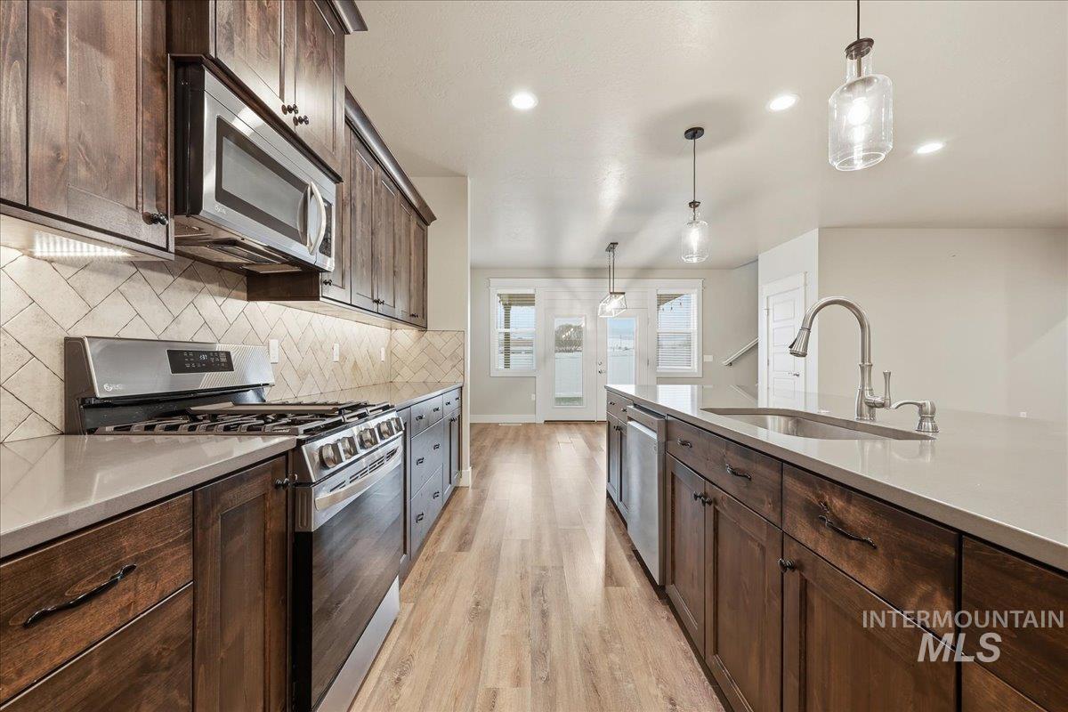 92 South Ravine Way Nampa, ID 83687 - Photo 9 of 29 Kitchen with appliances with stainless steel finishes, dark brown cabinets, decorative light fixtures, backsplash, and light stone counters