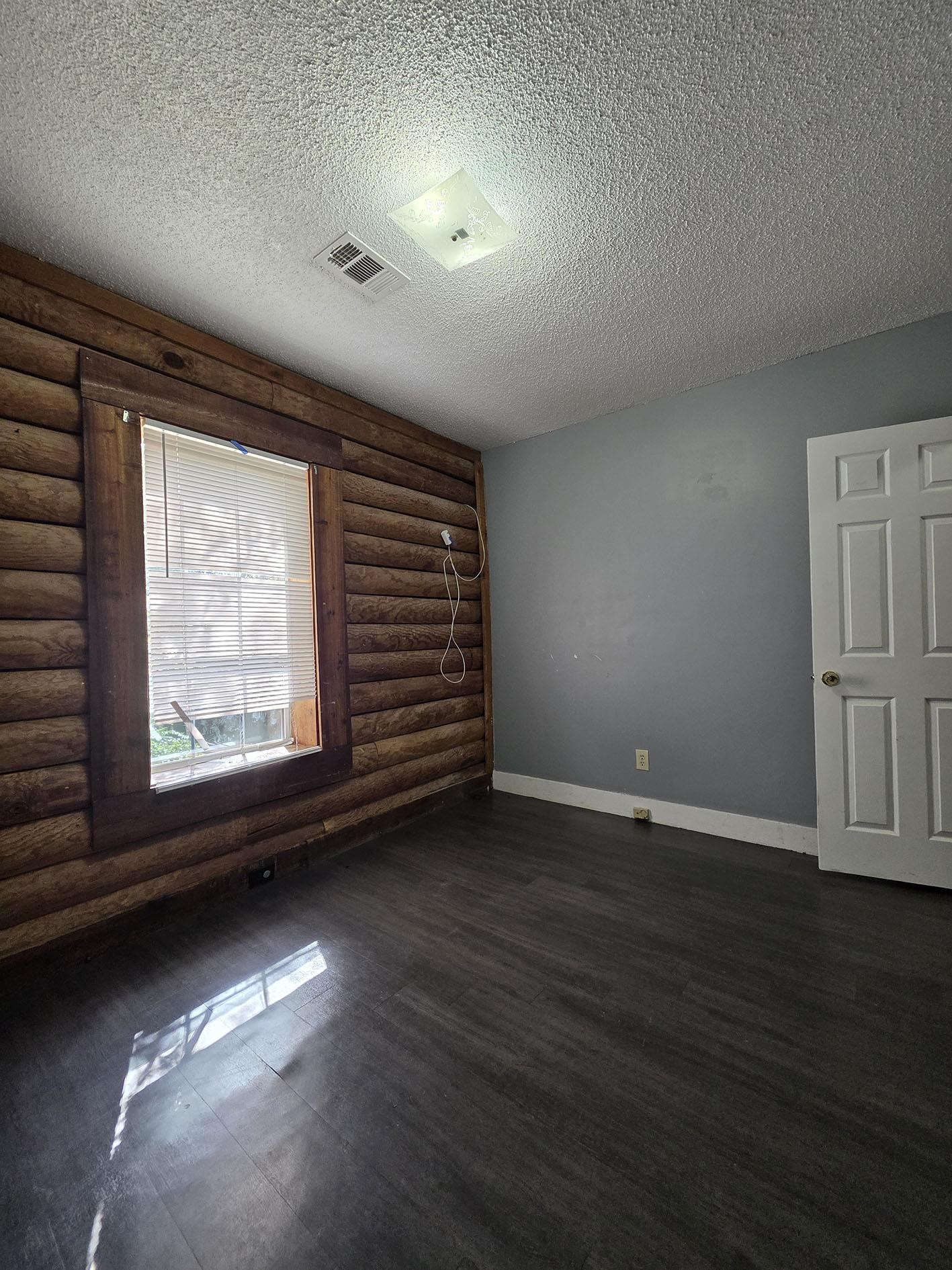 6521 Wimble Road Memphis, TN 38134 - Photo 11 of 18 Unfurnished room with a textured ceiling, dark wood-style flooring, and log walls