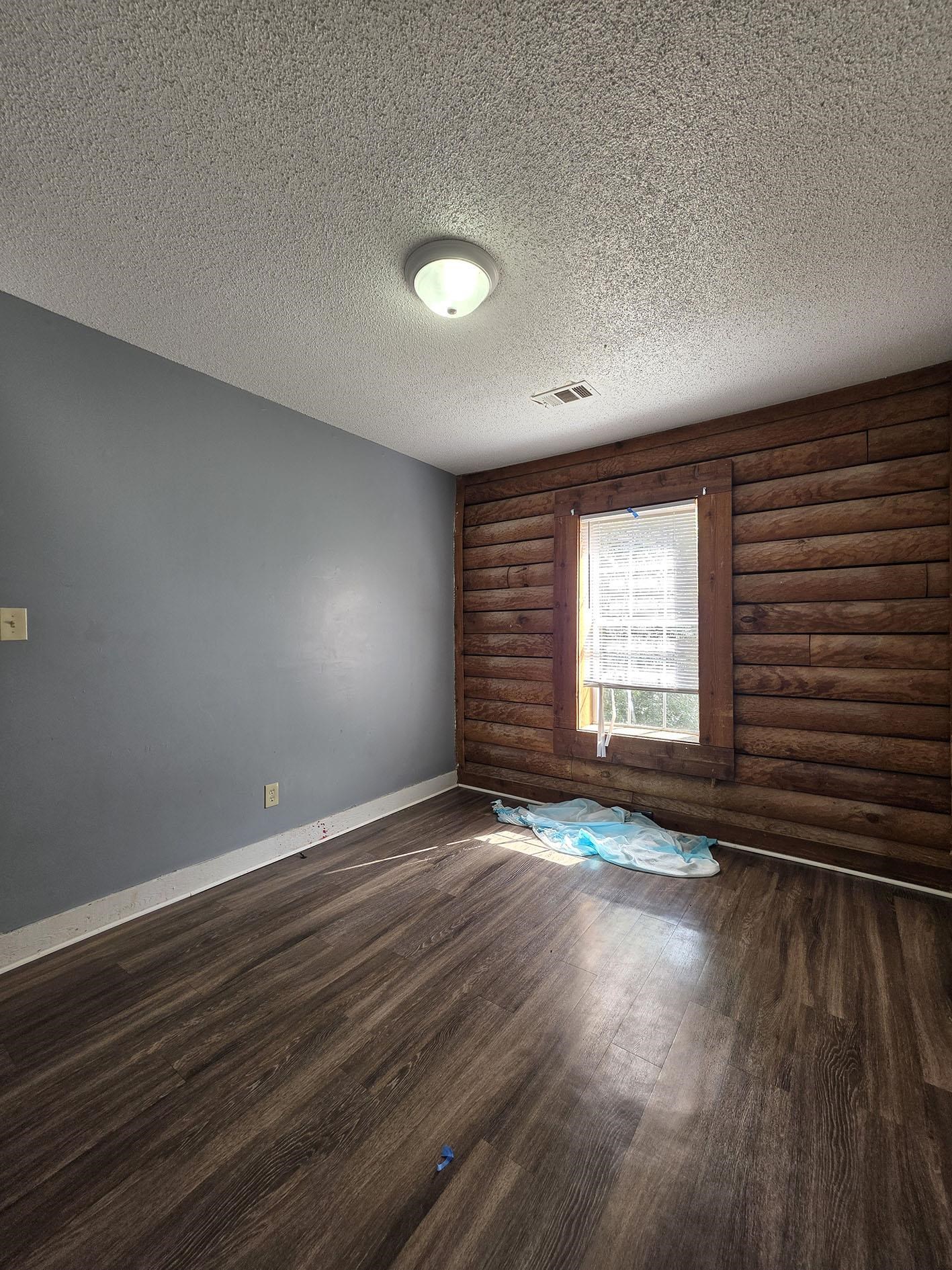 6521 Wimble Road Memphis, TN 38134 - Photo 12 of 18 Unfurnished room featuring log walls, dark wood-style floors, and a textured ceiling