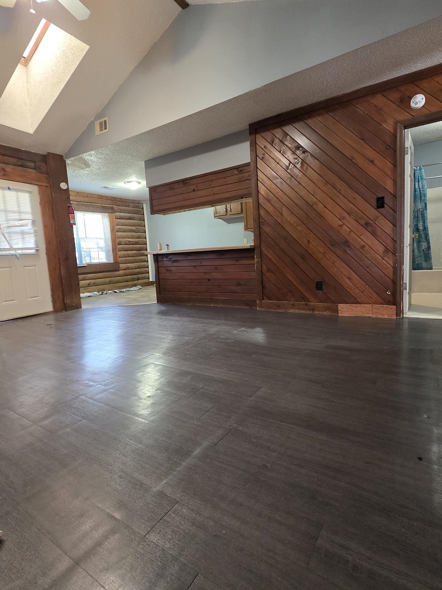 6521 Wimble Road Memphis, TN 38134 - Photo 3 of 18 Unfurnished living room featuring wood walls, a textured ceiling, vaulted ceiling, a skylight, and log walls