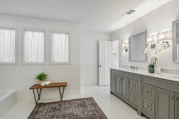 a spacious bathroom with double vanity sink a two mirror a window and a bathtub