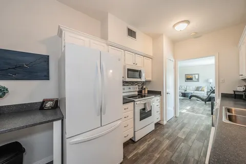 a kitchen with stainless steel appliances a stove a refrigerator a sink and white cabinets with wooden floor