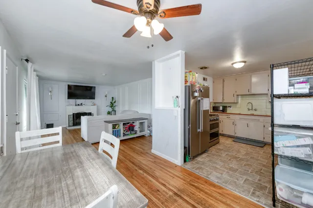 a kitchen view with stainless steel appliances kitchen island granite countertop a refrigerator a stove top oven a sink dishwasher and white cabinets with wooden floor