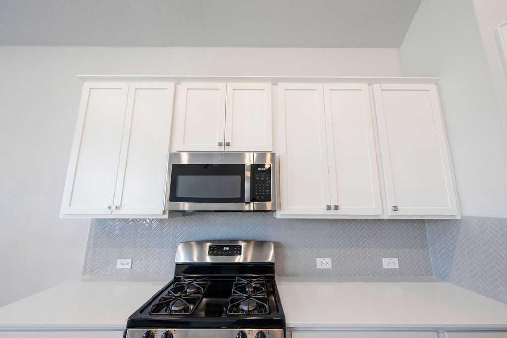 2032 Base Burner Path Leander, TX 78641 - Photo 28 of 34 Modern kitchen featuring white shaker-style cabinetry, stainless steel microwave, gas range, light-toned countertop, and herringbone tile backsplash