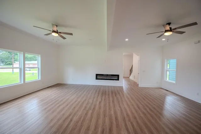 an empty room with wooden floor fan and windows