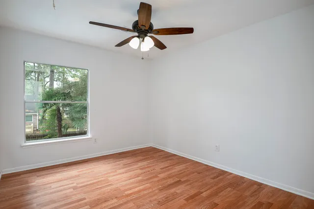 an empty room with wooden floor fan and windows