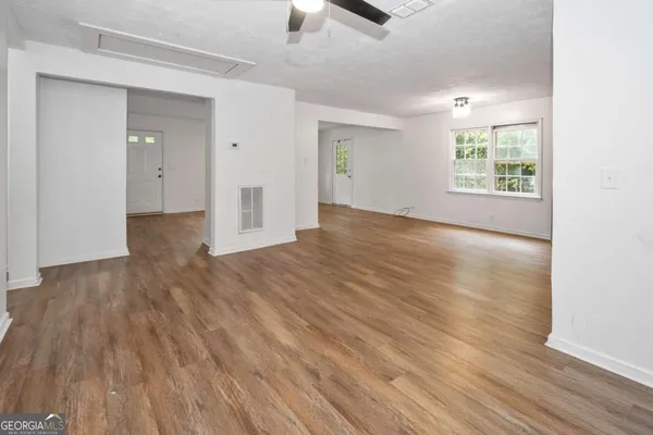 an empty room with wooden floor chandelier fan and windows