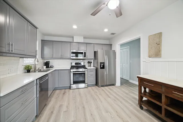 a kitchen with stainless steel appliances a stove top oven a sink dishwasher and a refrigerator with wooden floor