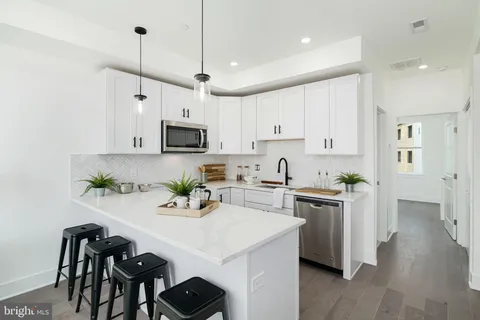 a kitchen with stainless steel appliances a stove a sink a microwave a refrigerator and white cabinets with wooden floor