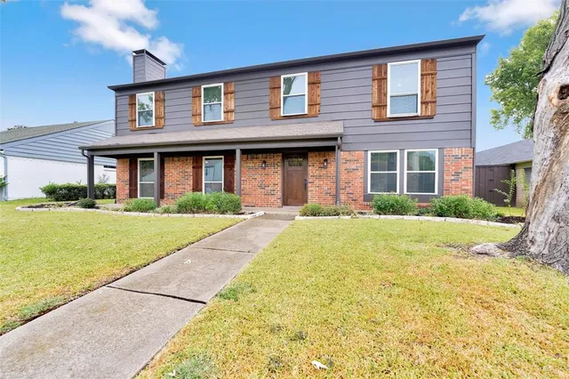 a brick house with a big yard plants and palm trees