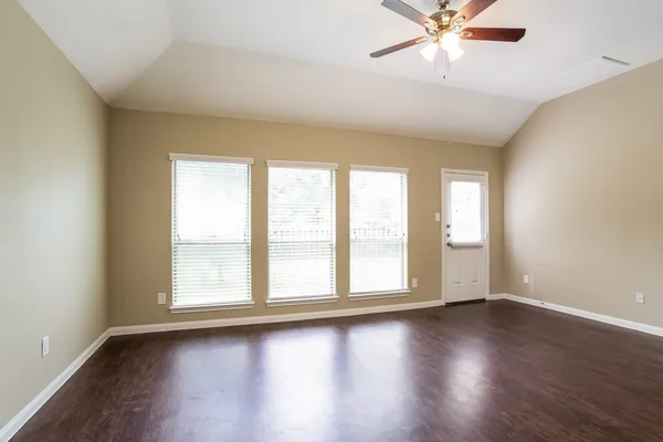 an empty room with wooden floor fan and windows
