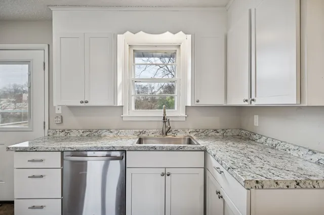 a kitchen with granite countertop white cabinets sink and window