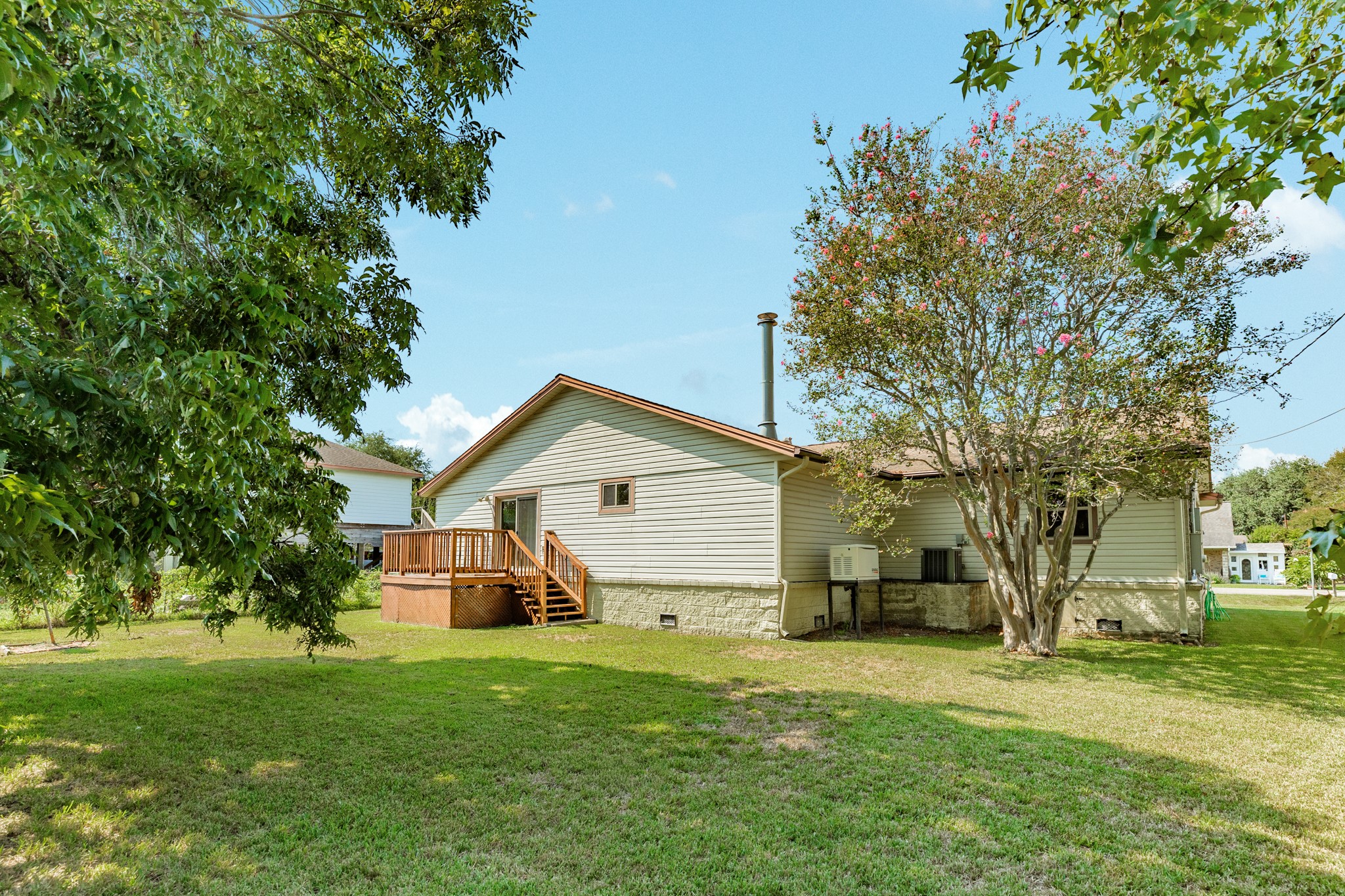 616 Bel Road Kemah, TX 77565 - Photo 17 of 23 Spacious backyard provides abundant green space surrounded by mature trees, offering plenty of room for outdoor activities, gardening, or entertaining. A raised wood deck with stairs overlooks the yard and creates a convenient outdoor gathering space directly accessible from the home.