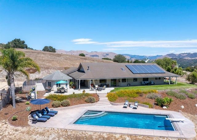 a view of a big house with pool and lawn chairs under an umbrella