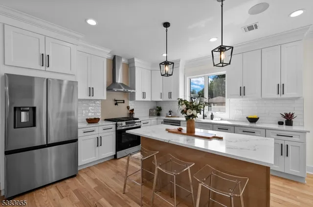 a kitchen with stainless steel appliances granite countertop a sink a stove a refrigerator and white cabinets with wooden floor