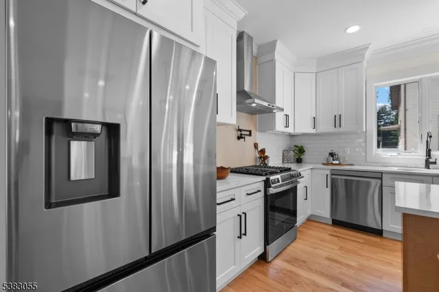 a kitchen with stainless steel appliances granite countertop a stove top oven a refrigerator and white cabinets with wooden floor