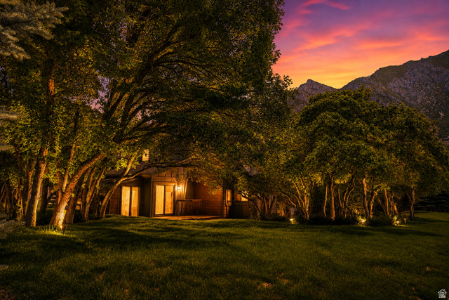 578 High Bench Road Alpine, UT 84004 - Photo 37 of 39 Exterior featuring a mountainous backdrop, mature trees with uplighting, a manicured lawn, and a private patio with exterior lighting