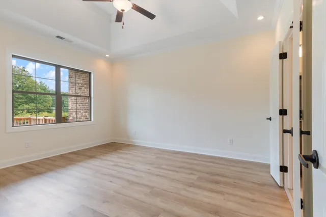 an empty room with wooden floor chandelier fan and windows