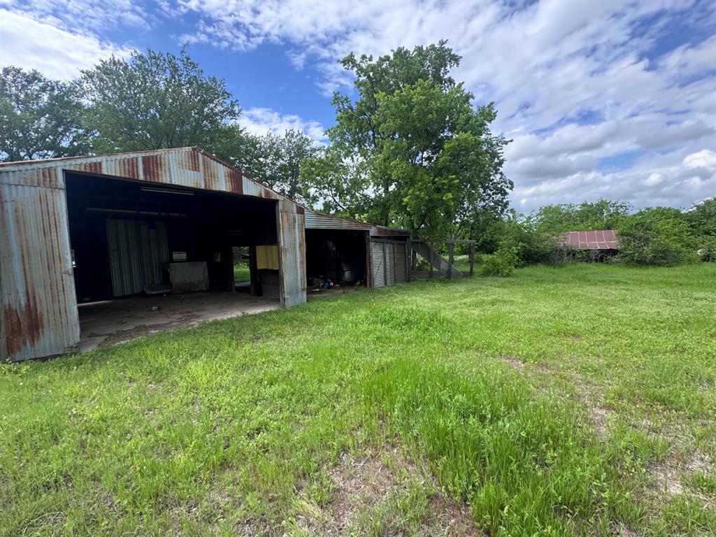 1210 Old Chico Road Decatur, TX 76234 - Photo 9 of 9 Corrugated metal outbuilding with multiple bays and concrete flooring, surrounded by a grassy area and mature trees