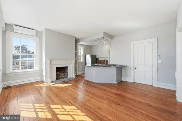 a view of kitchen and empty room with wooden floor and fireplace