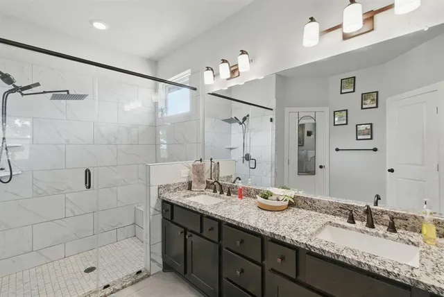 a bathroom with a granite countertop double vanity sink mirror and shower