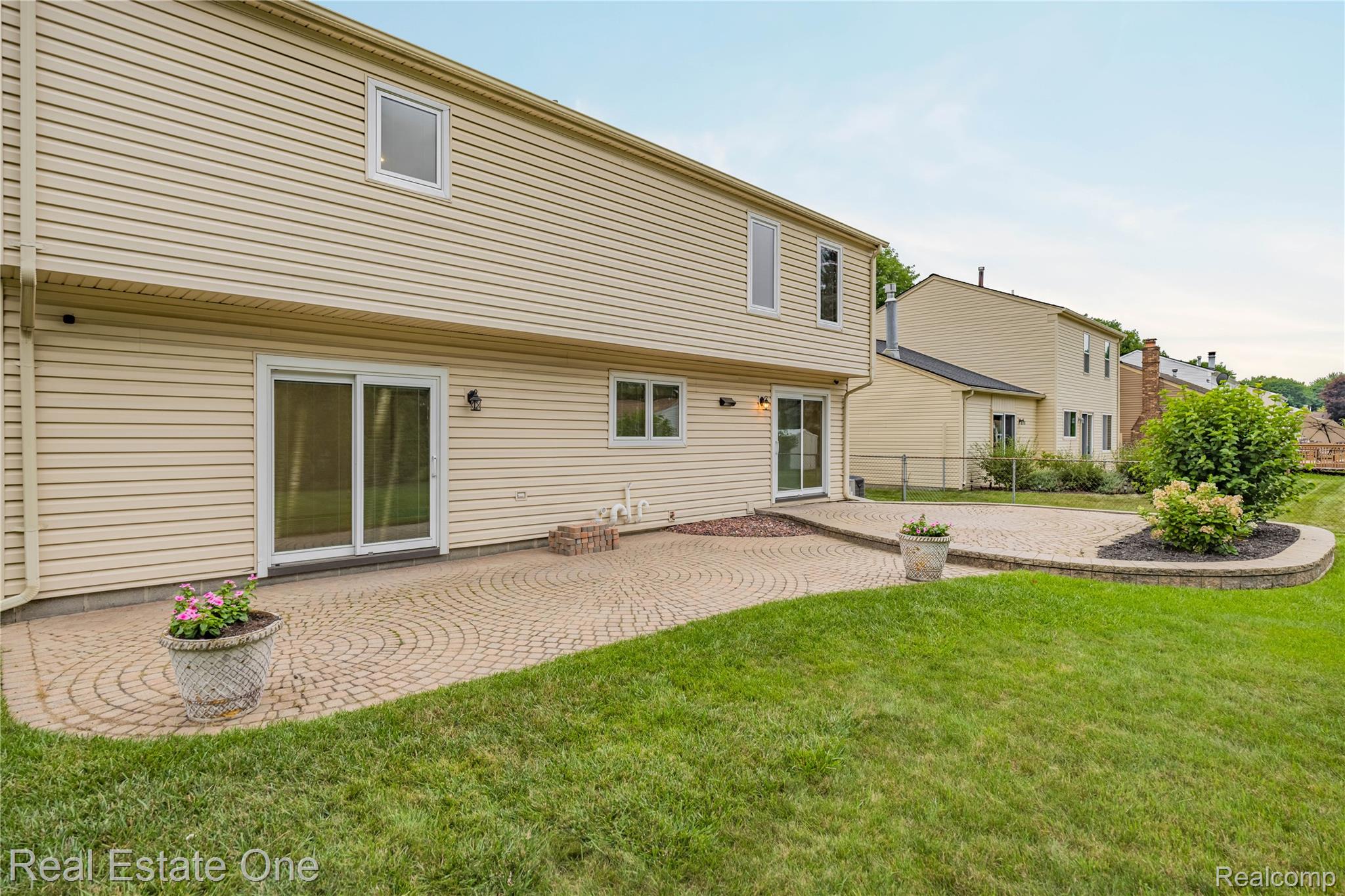 39750 Cheviot Road Canton, MI 48188 - Photo 65 of 71 Expansive paver patio with a radial pattern, featuring a raised garden bed and direct access via dual sliding glass doors
