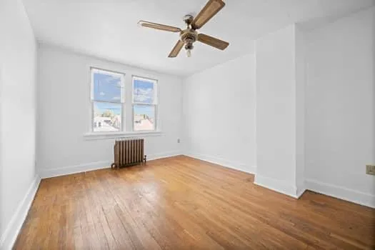 an empty room with wooden floor chandelier fan and windows