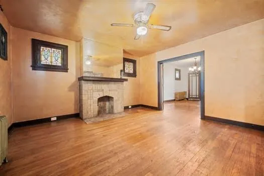 a view of a livingroom with a fireplace a ceiling fan and wooden floor