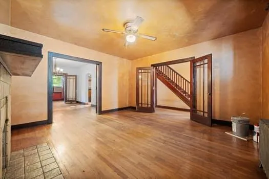 a view of an empty room with wooden floor and a ceiling fan