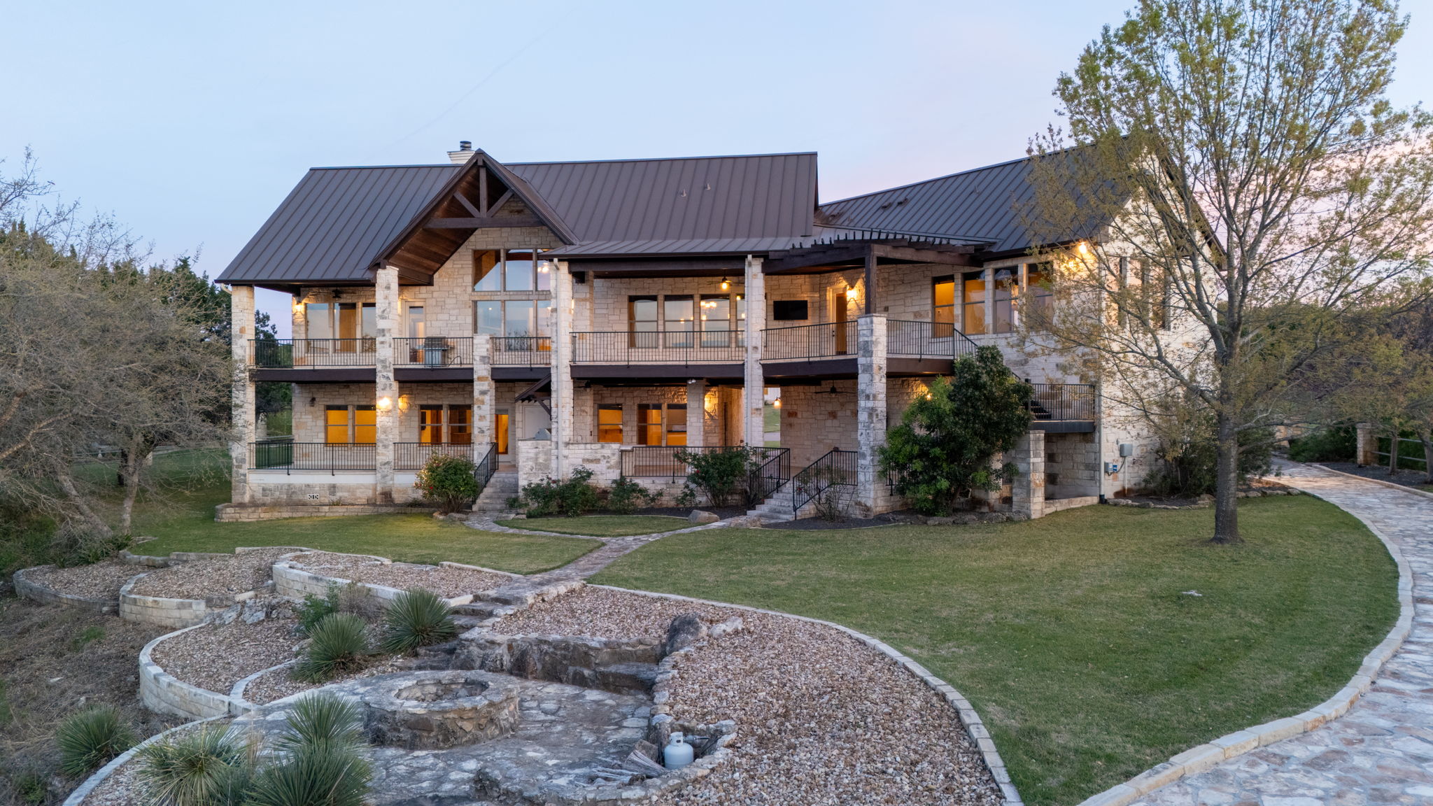 5010 Lookout Ridge Drive Marble Falls, TX 78654 - Photo 8 of 40 Back of house at dusk featuring stone siding, a standing seam roof, a yard, and a balcony