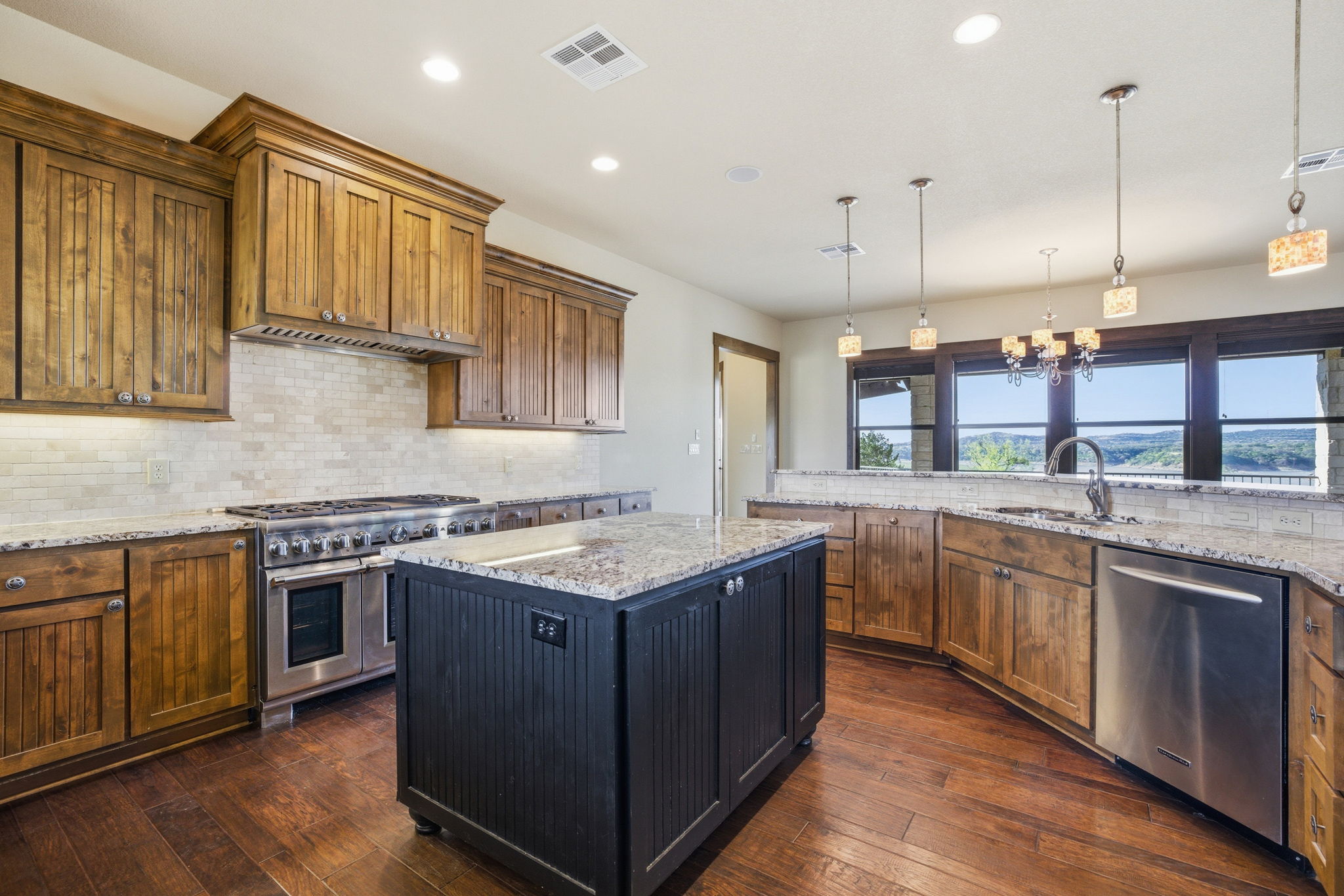 5010 Lookout Ridge Drive Marble Falls, TX 78654 - Photo 17 of 40 Kitchen with light stone counters, stainless steel appliances, a kitchen island, wood finish cabinets, and dark wood-style flooring