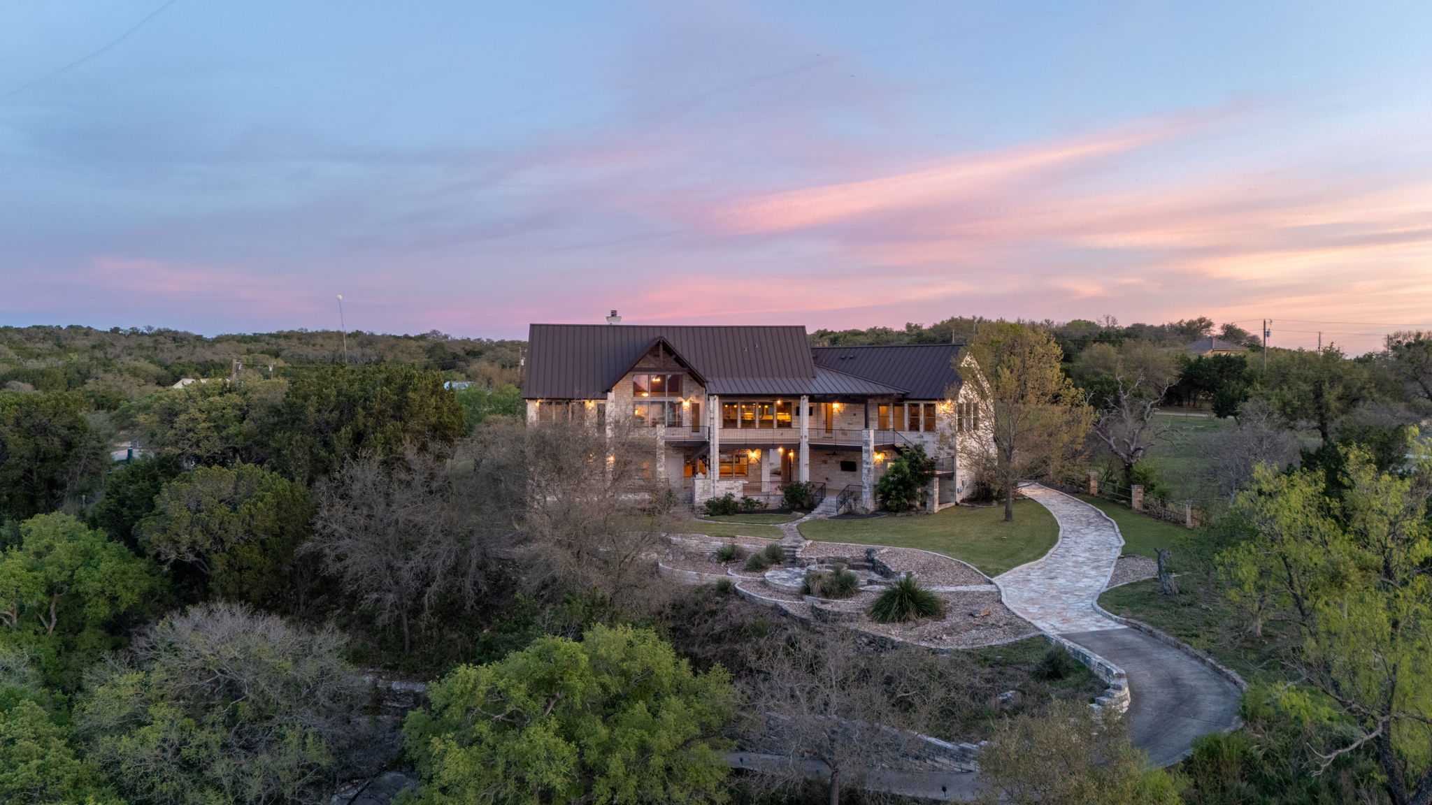 5010 Lookout Ridge Drive Marble Falls, TX 78654 - Photo 33 of 40 Back of house at dusk featuring a metal roof, a lawn, and stone siding