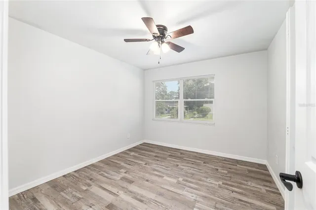 an empty room with wooden floor fan and windows