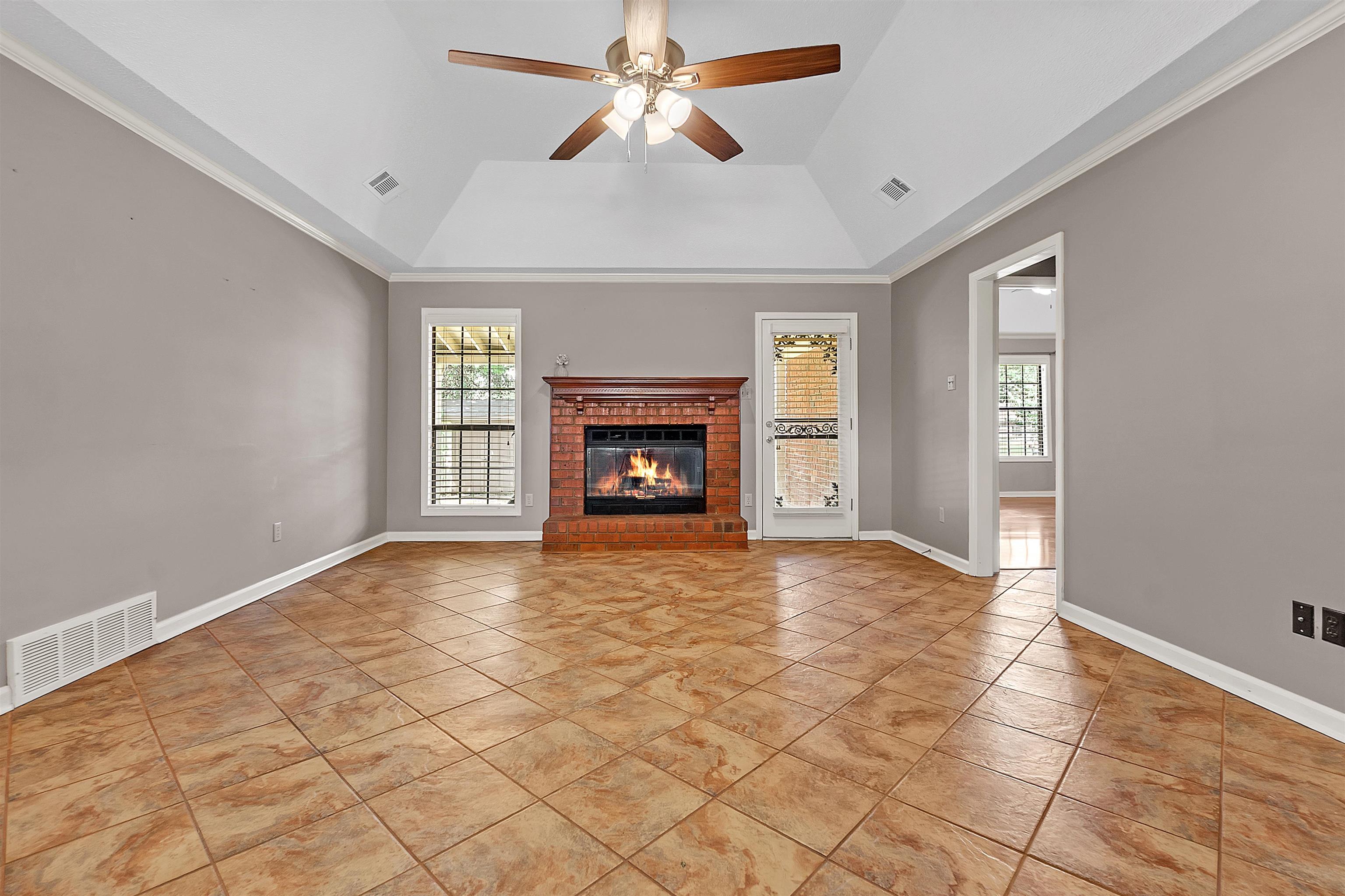 6512 Birch Mill Road Bartlett, TN 38135 - Photo 3 of 25 Unfurnished living room featuring a ceiling fan, ornamental molding, a brick fireplace, lofted ceiling, and light tile patterned flooring