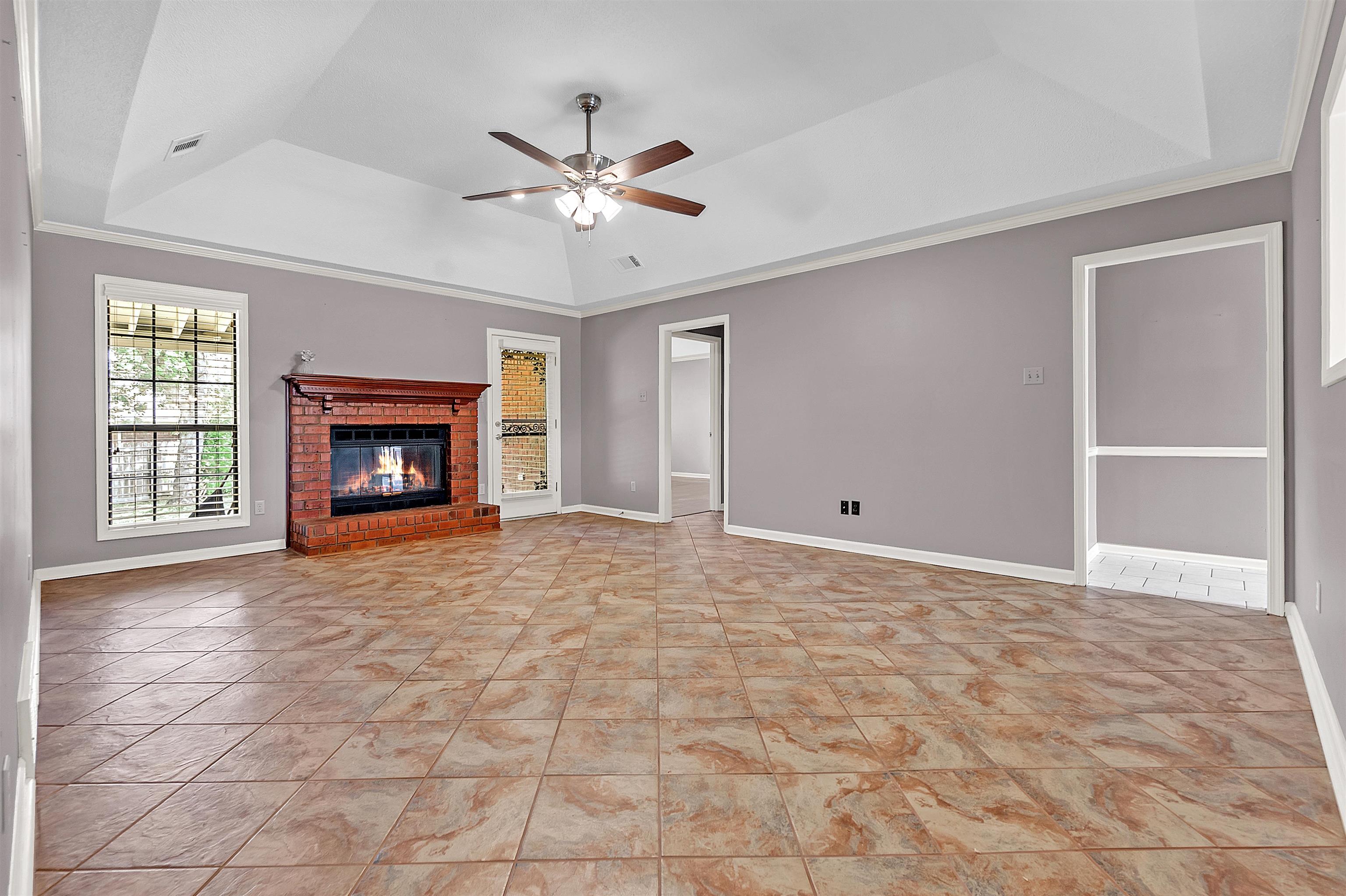 6512 Birch Mill Road Bartlett, TN 38135 - Photo 6 of 25 Unfurnished living room featuring a tray ceiling, ceiling fan, a brick fireplace, crown molding, and light tile patterned floors