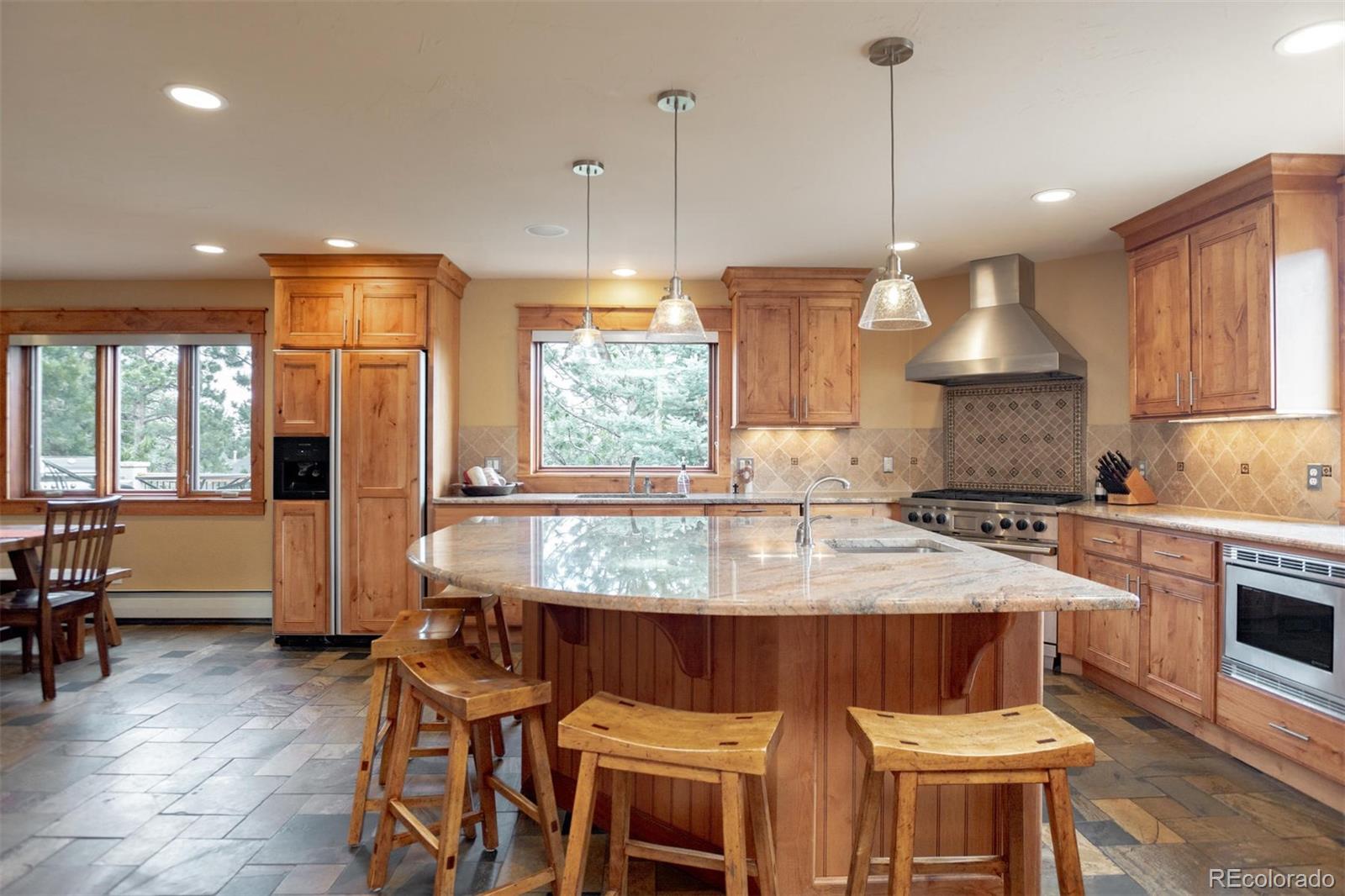33231 Meadow Mountain Road Evergreen, CO 80439 - Photo 6 of 40 a kitchen with stainless steel appliances granite countertop a stove a refrigerator a sink a dining table and chairs with wooden floor