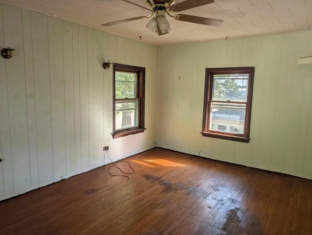 an empty room with wooden floor chandelier fan and windows