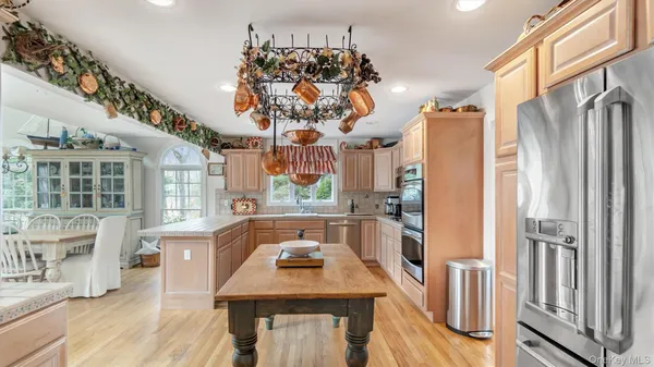 a kitchen with stainless steel appliances granite countertop a refrigerator a sink dishwasher a stove and a dining table with wooden floor