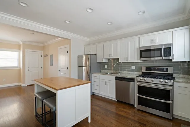 a kitchen with stainless steel appliances a stove a sink dishwasher a refrigerator white cabinets and wooden floor