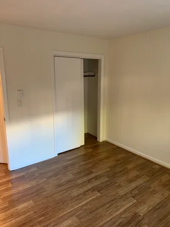 a view of an empty room with wooden floor and closet